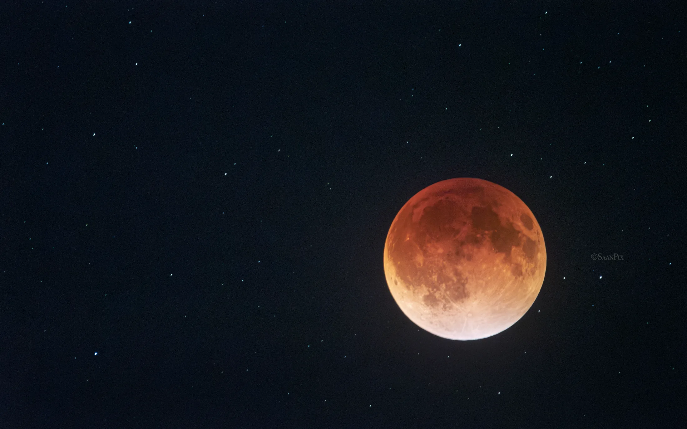 Copper-red eclipsed Moon surrounded by stars