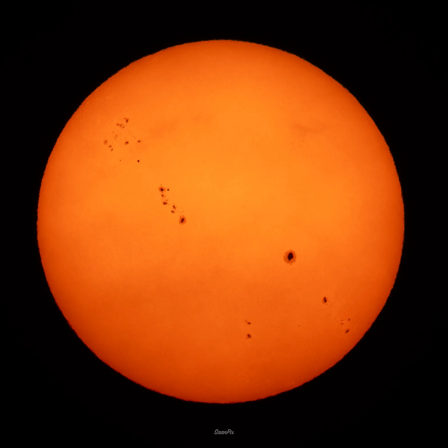 Orange solar disc with several visible sunspot groups