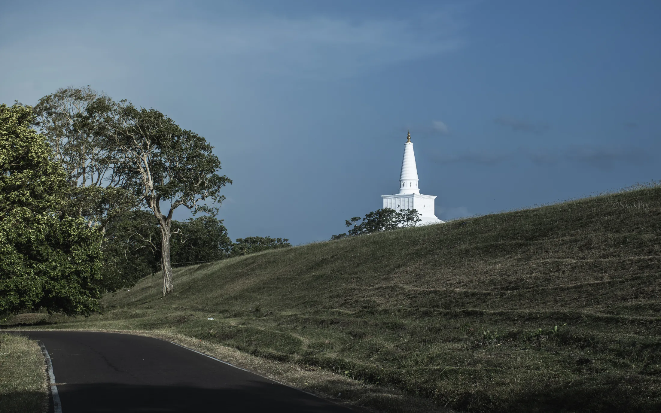 White stupa on a hill beside a curving road