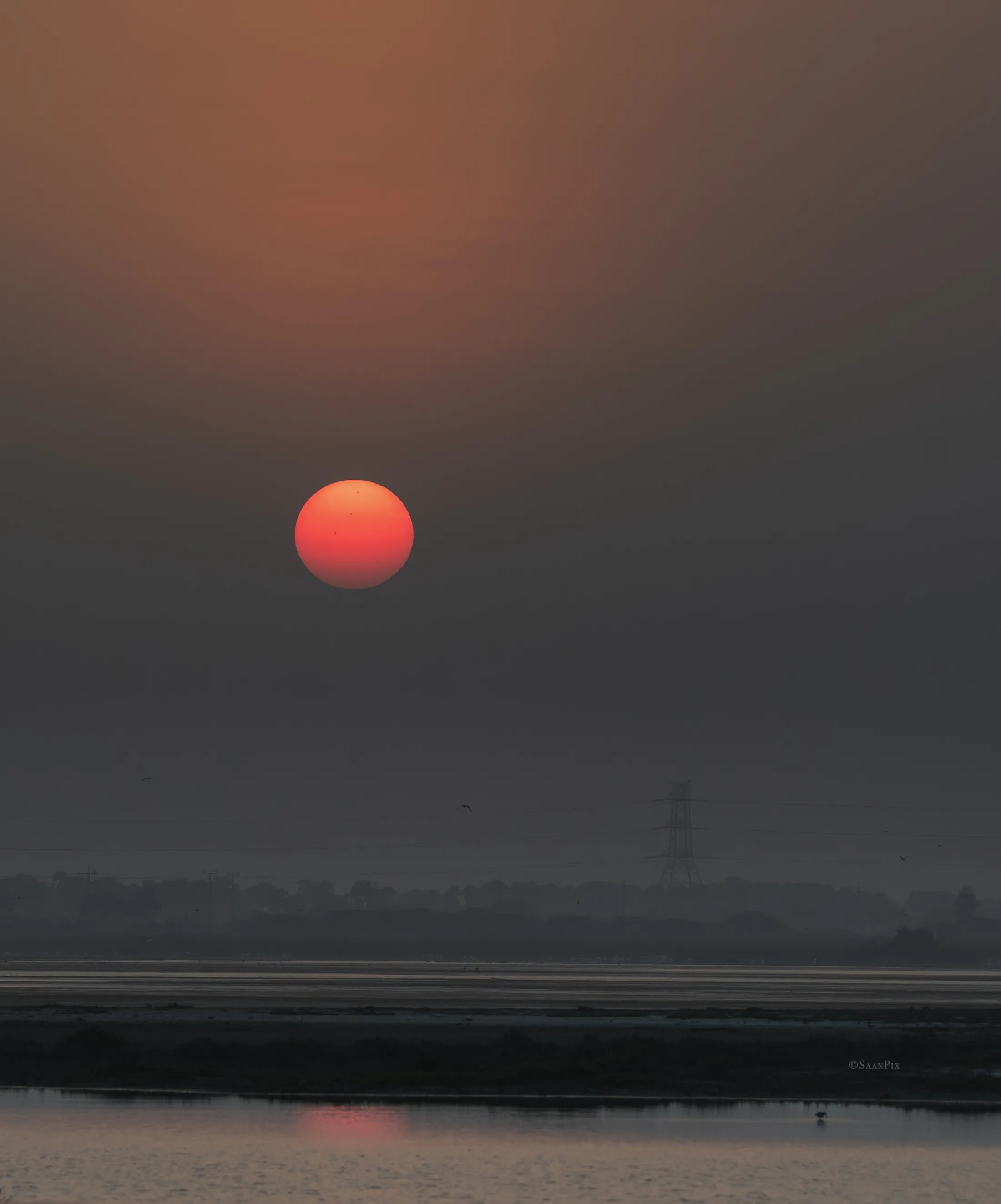 Red sun descending through haze above water